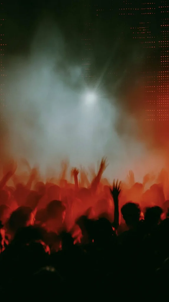 A blurred red-lit club crowd with raised hands under pale haze and a bright strobe, grainy 35mm film