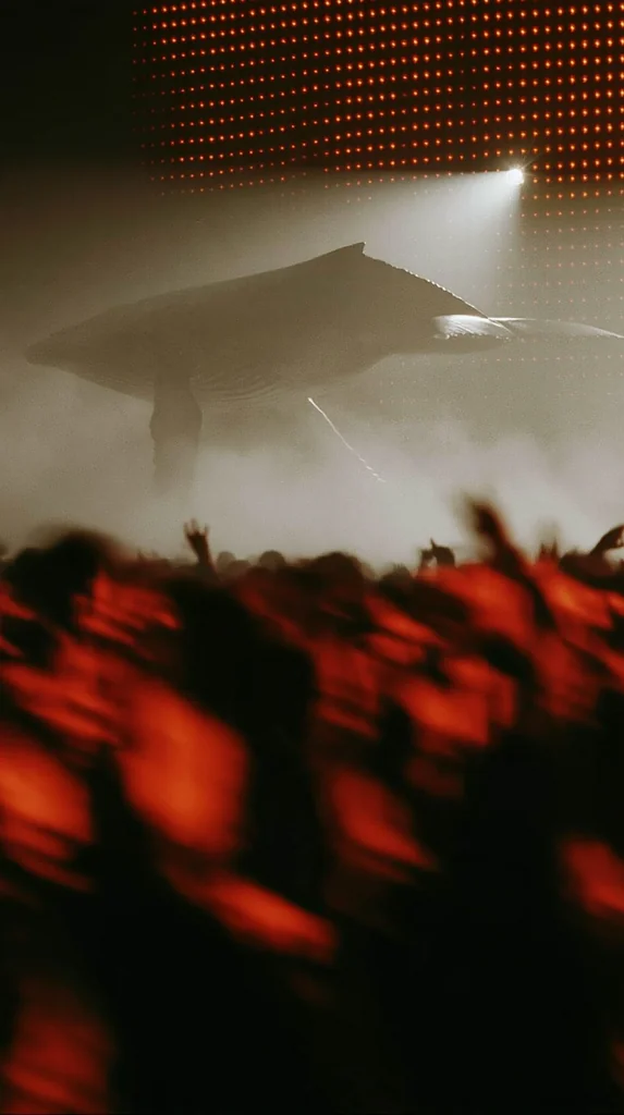 A whale looming in pale haze above a red-lit blurred club crowd, grainy film photo