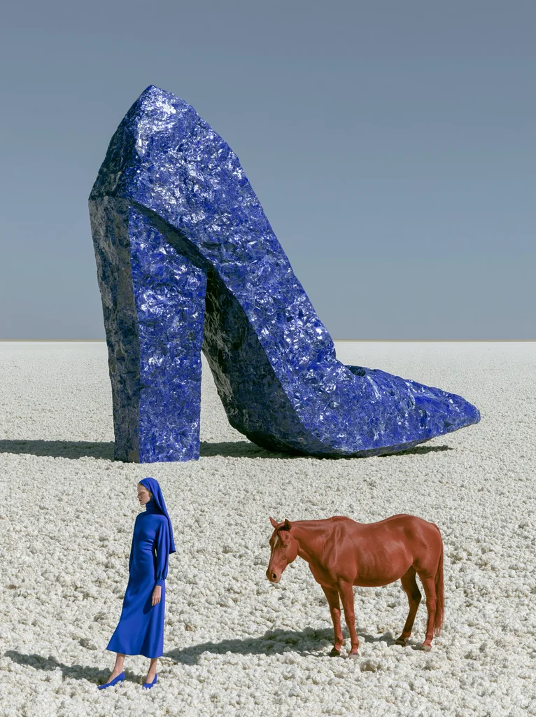 A colossal high-heeled shoe of cobalt mineral on a salt flat, with a woman in blue and a red horse