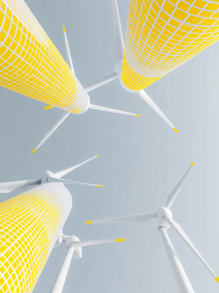 White wind turbines with lemon yellow towers seen from below against a pale gray sky